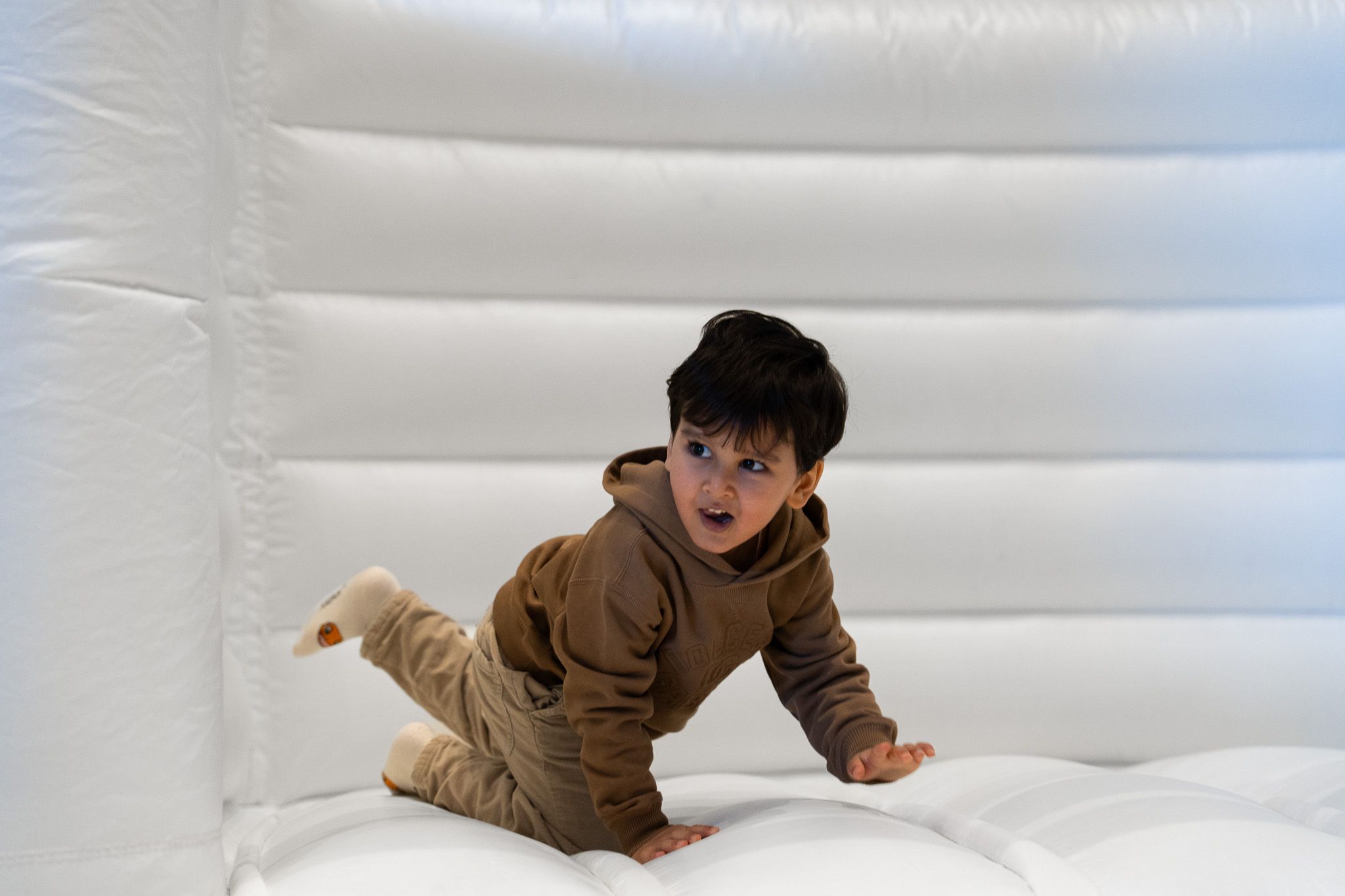 Toddler boy in brown hoodie playing inside a white inflatable bouncy castle during a kids birthday party in Auckland
