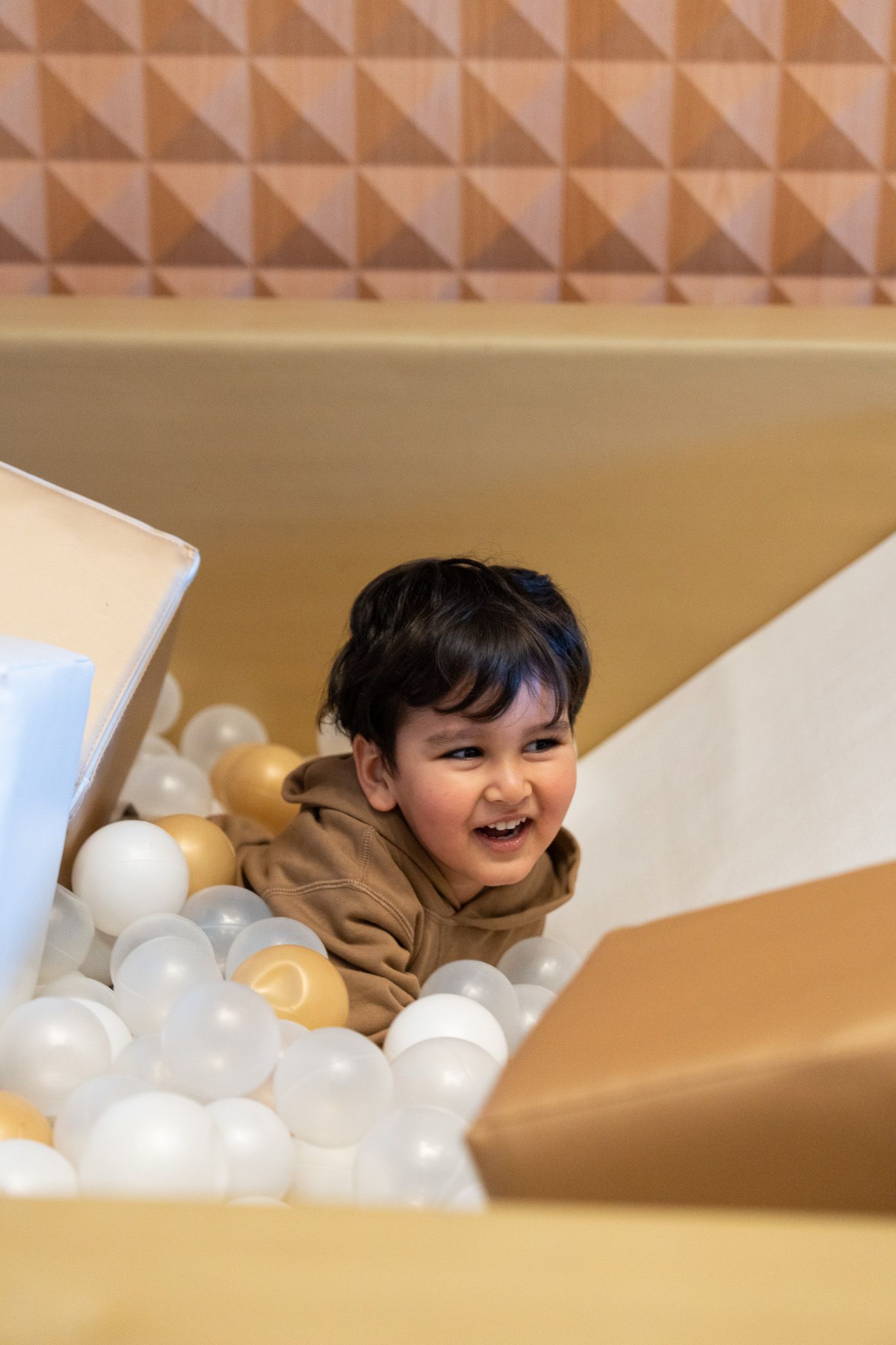 Close-up of a laughing toddler surrounded by gold and white plastic balls in a stylish ball pit at a birthday party in Auckland