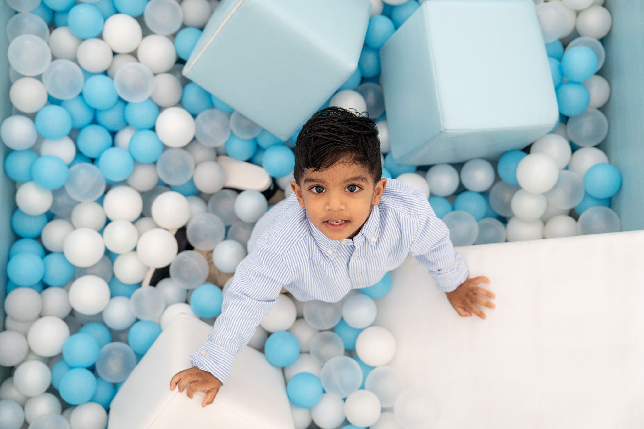 Ahan looking up from a blue and white ball pit, surrounded by soft play blocks and colourful play balls