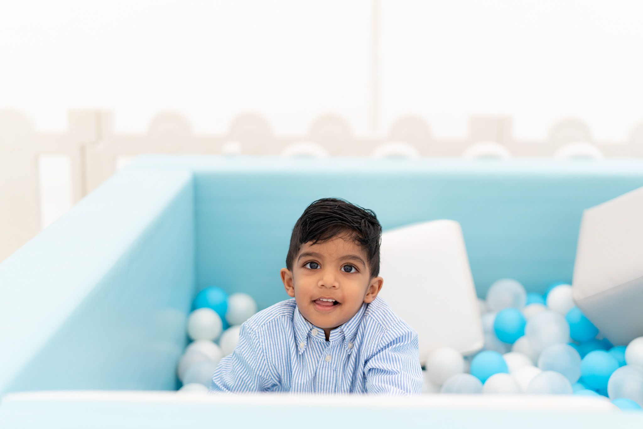 Ahan sitting in ball pit smiling during pastel themed second birthday party kids birthday photography in Auckland