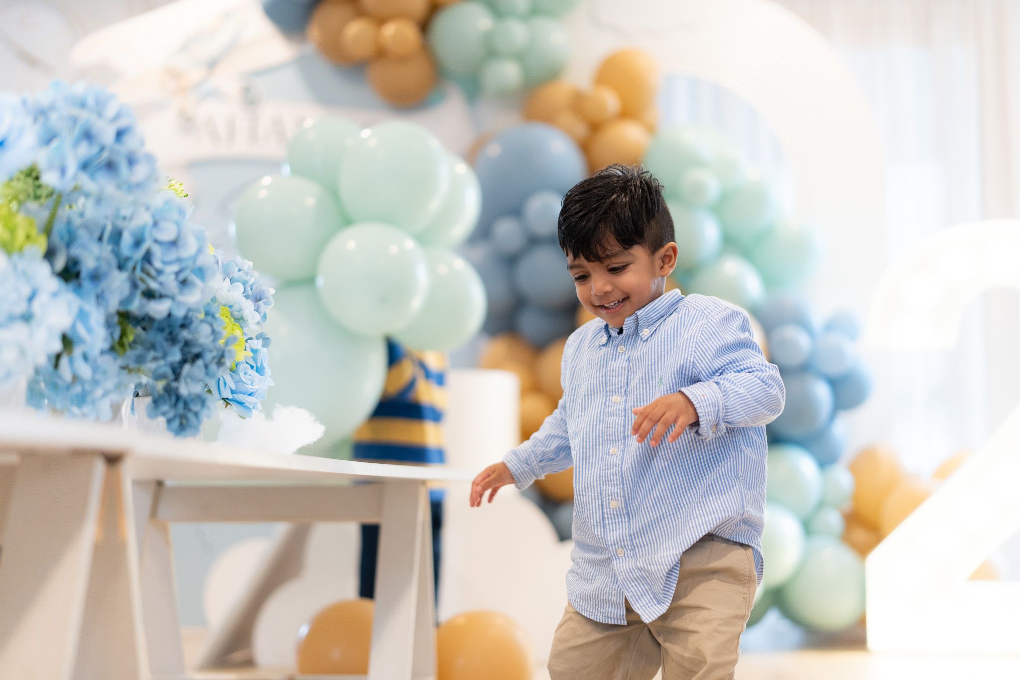 Toddler Ahan walking near decorated birthday table with balloons and travel themed decor second birthday photography in Auckland
