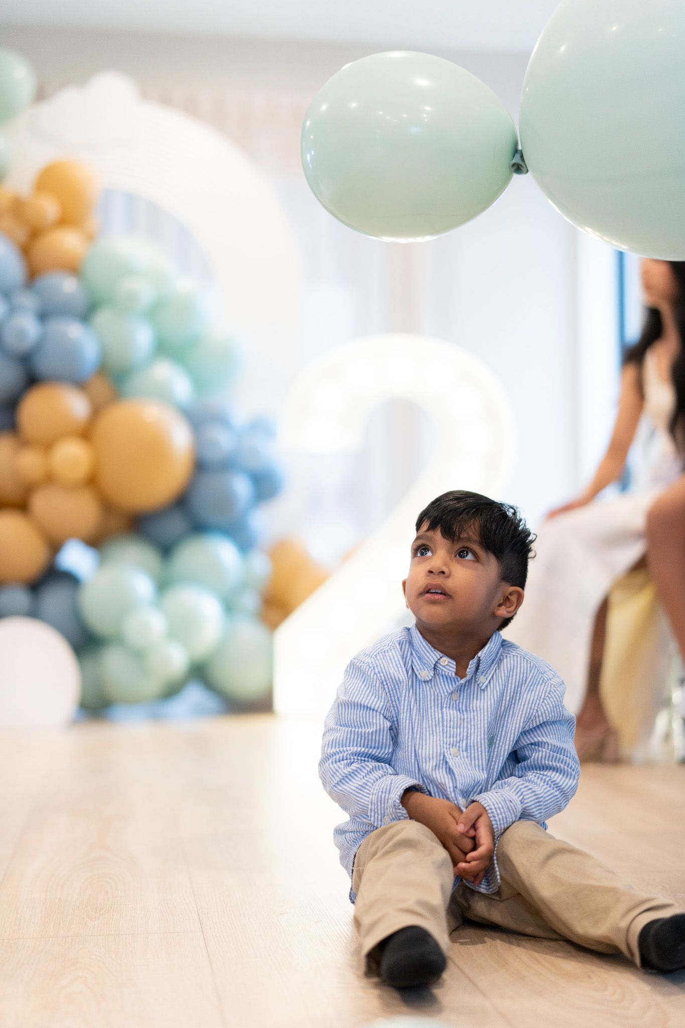 Ahan sitting on floor looking at balloons during pastel travel themed second birthday celebration photography in Auckland