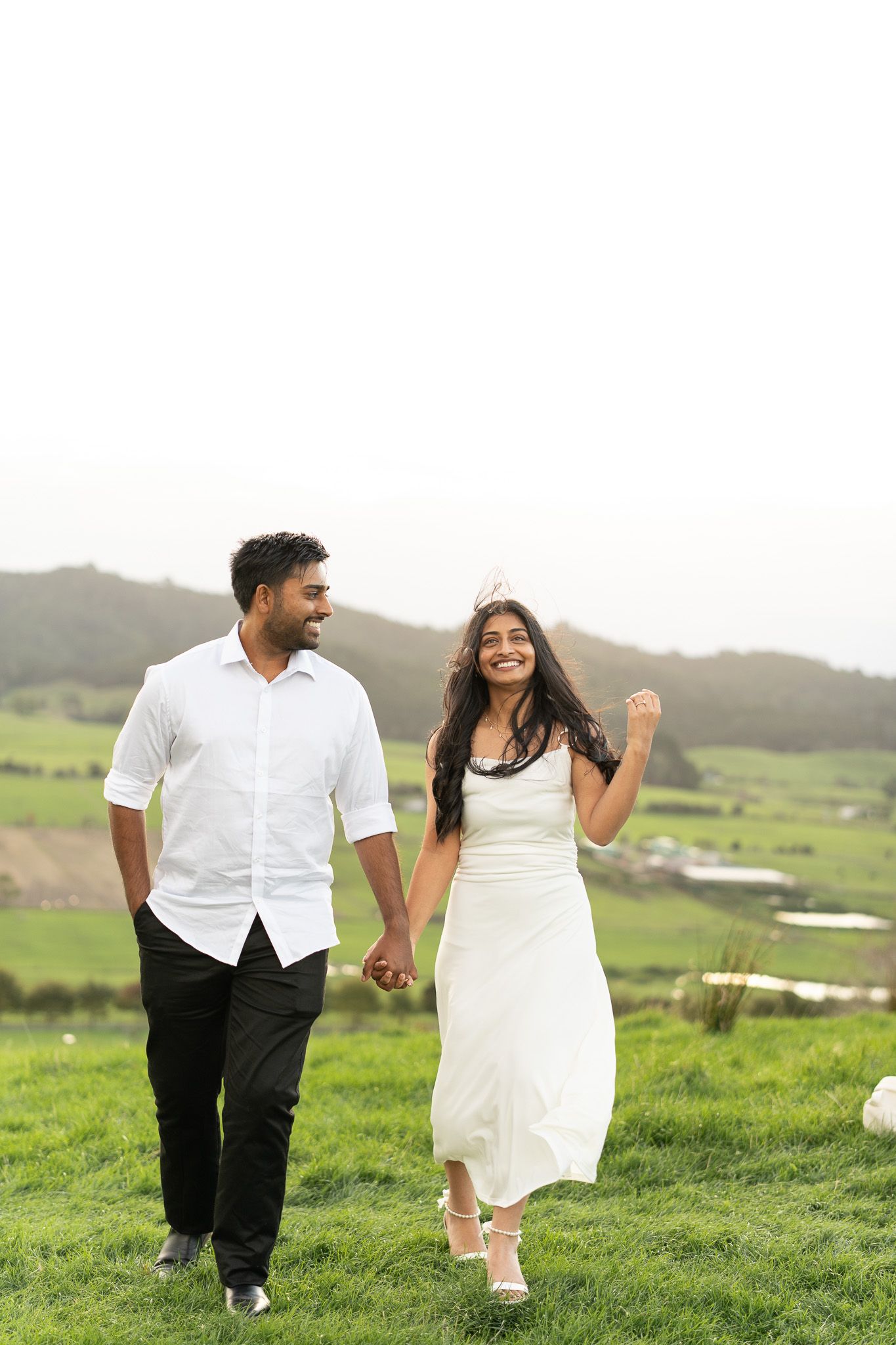 Amish and Komal walking hand in hand through long grass at Duders Regional Park during a relaxed couples shoot