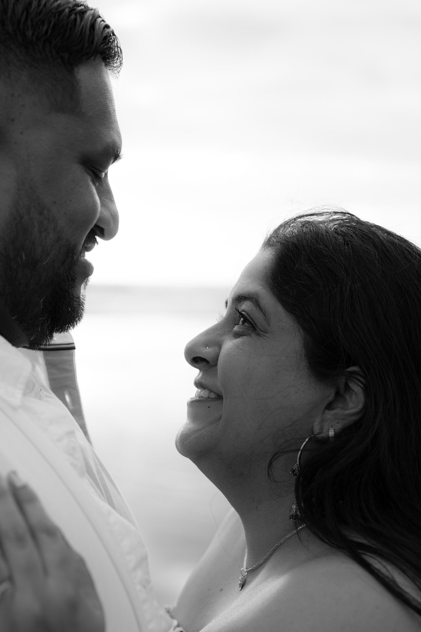 Close-up black and white portrait of smiling woman looking lovingly at her partner during a beach engagement photography shoot in Auckland