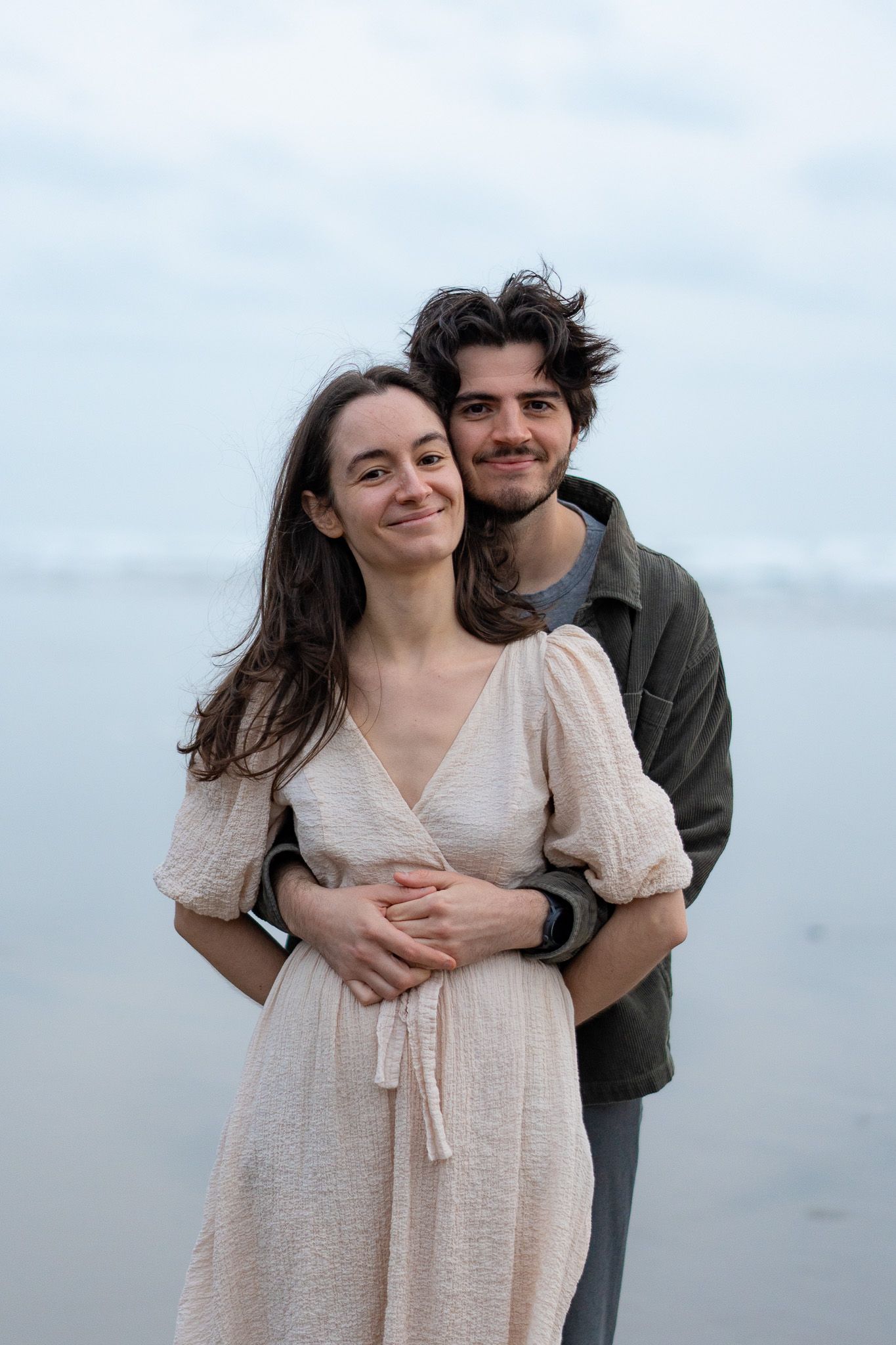 Couple embracing closely with soft natural light and ocean breeze during an intimate and romantic beach photoshoot in Auckland