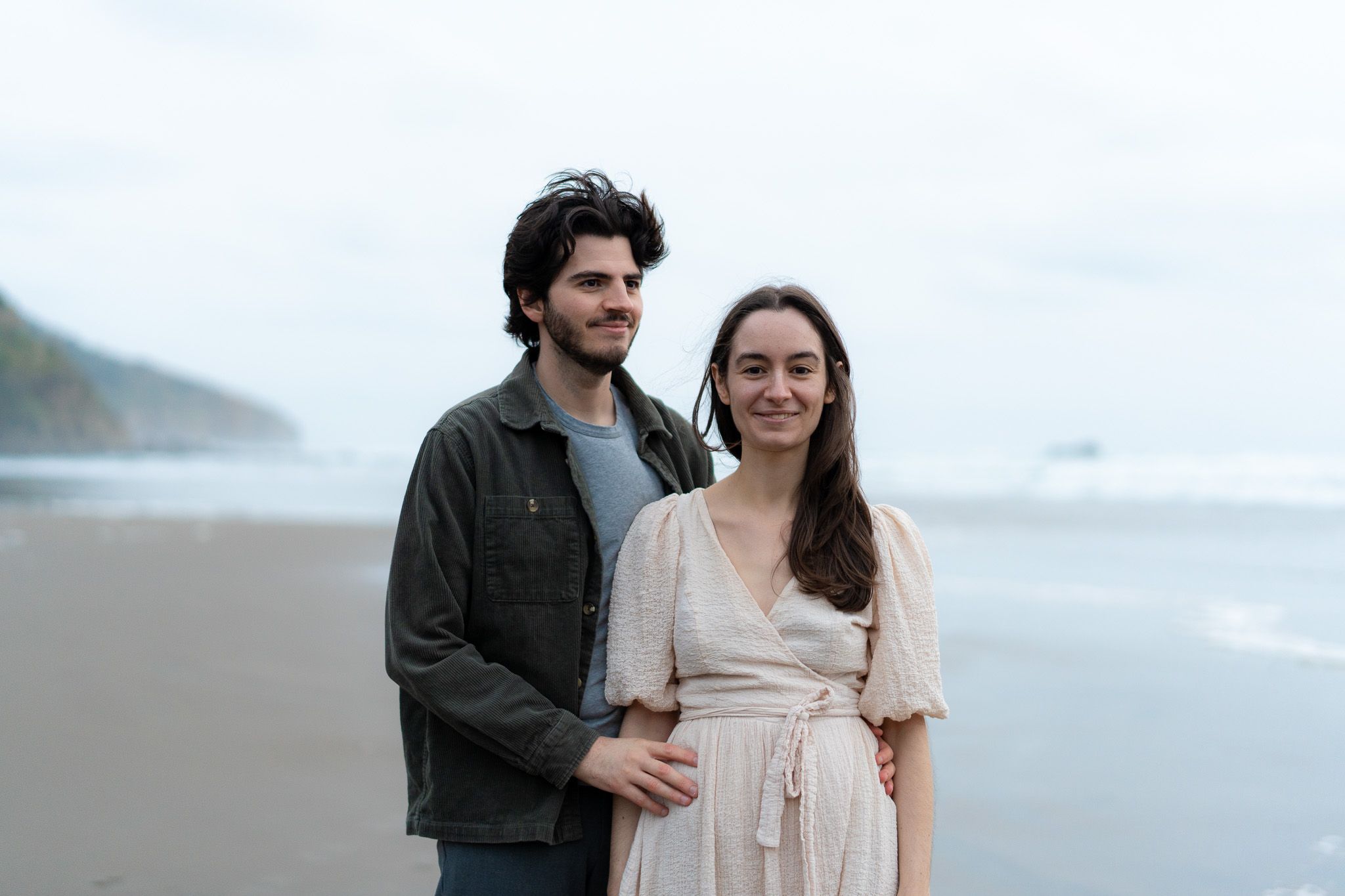 Couple standing side by side on the sand looking softly toward the distance during a serene beach photography session in Auckland
