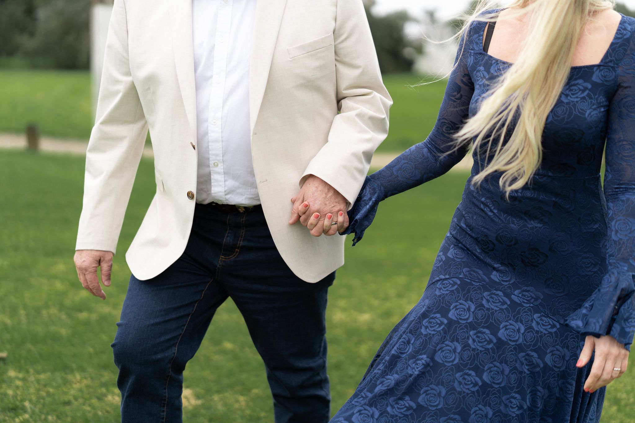 Close-up of the bride and groom holding hands as they walk across the grass