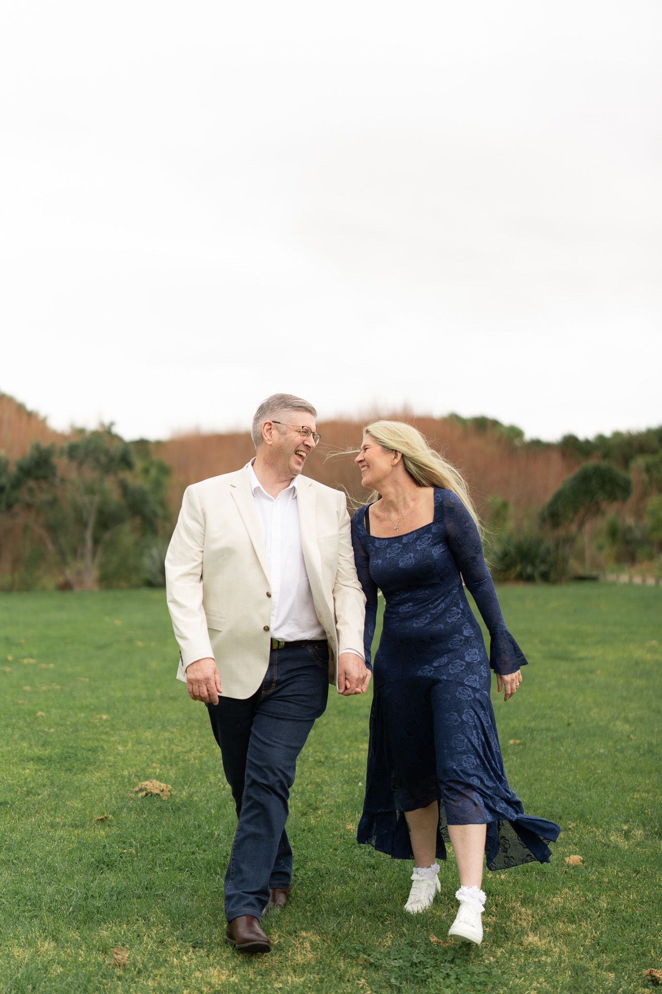 Bride and groom laughing together nose to nose while walking across the grass