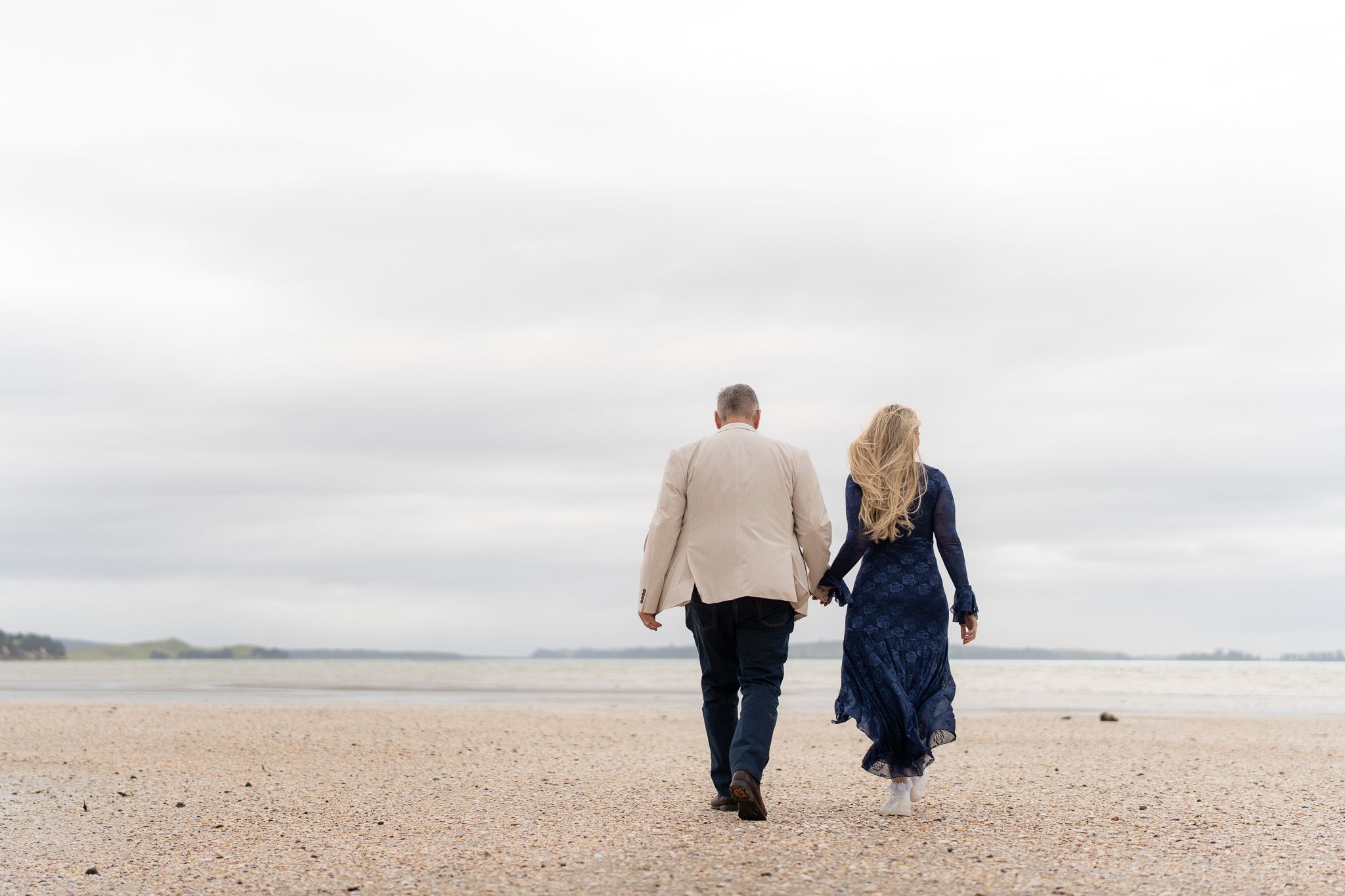 Bride and groom walking hand in hand along the beach at Musick Point, Auckland