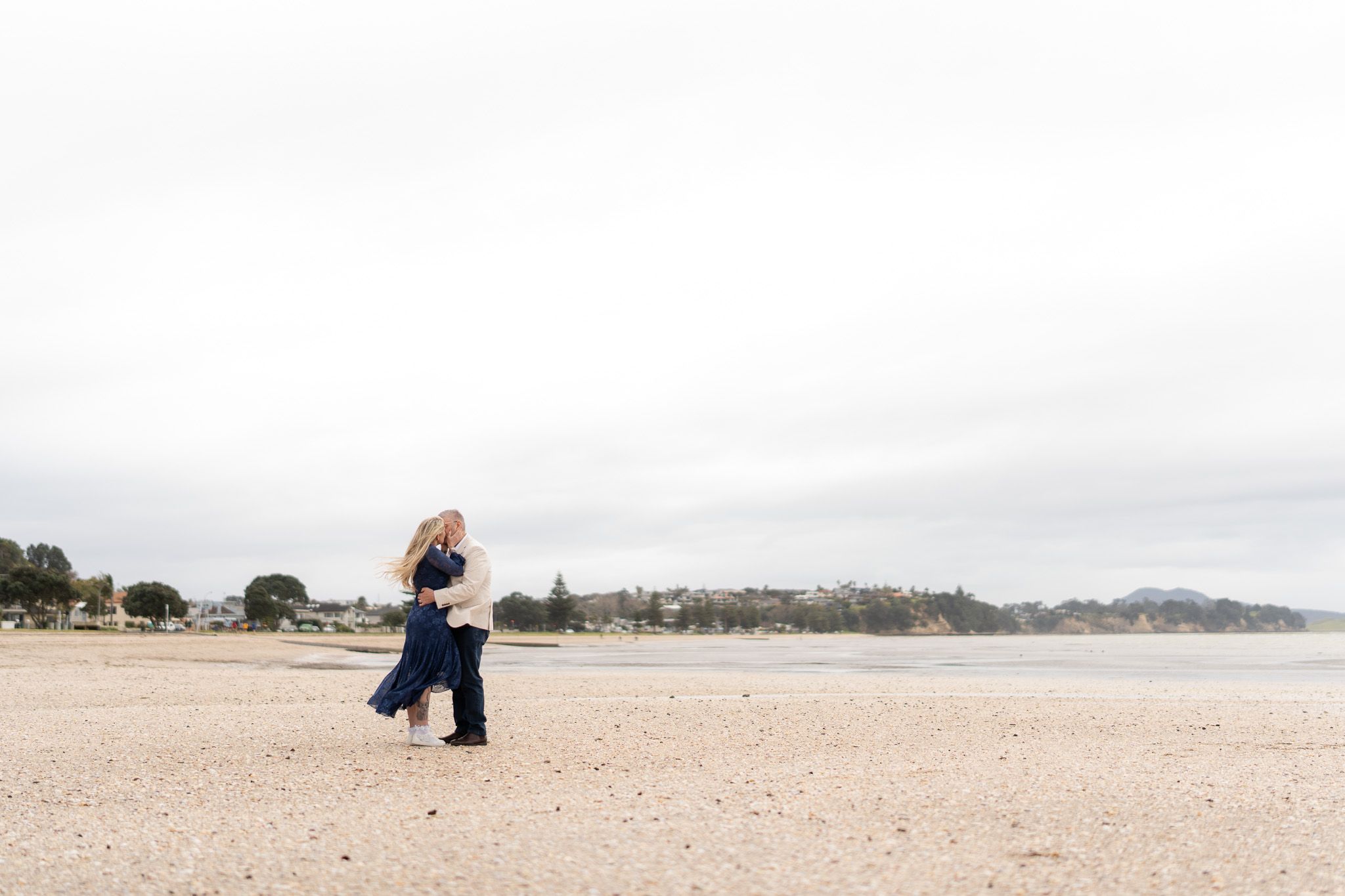 Bride and groom embracing on the beach with the Musick Point coastline in the background