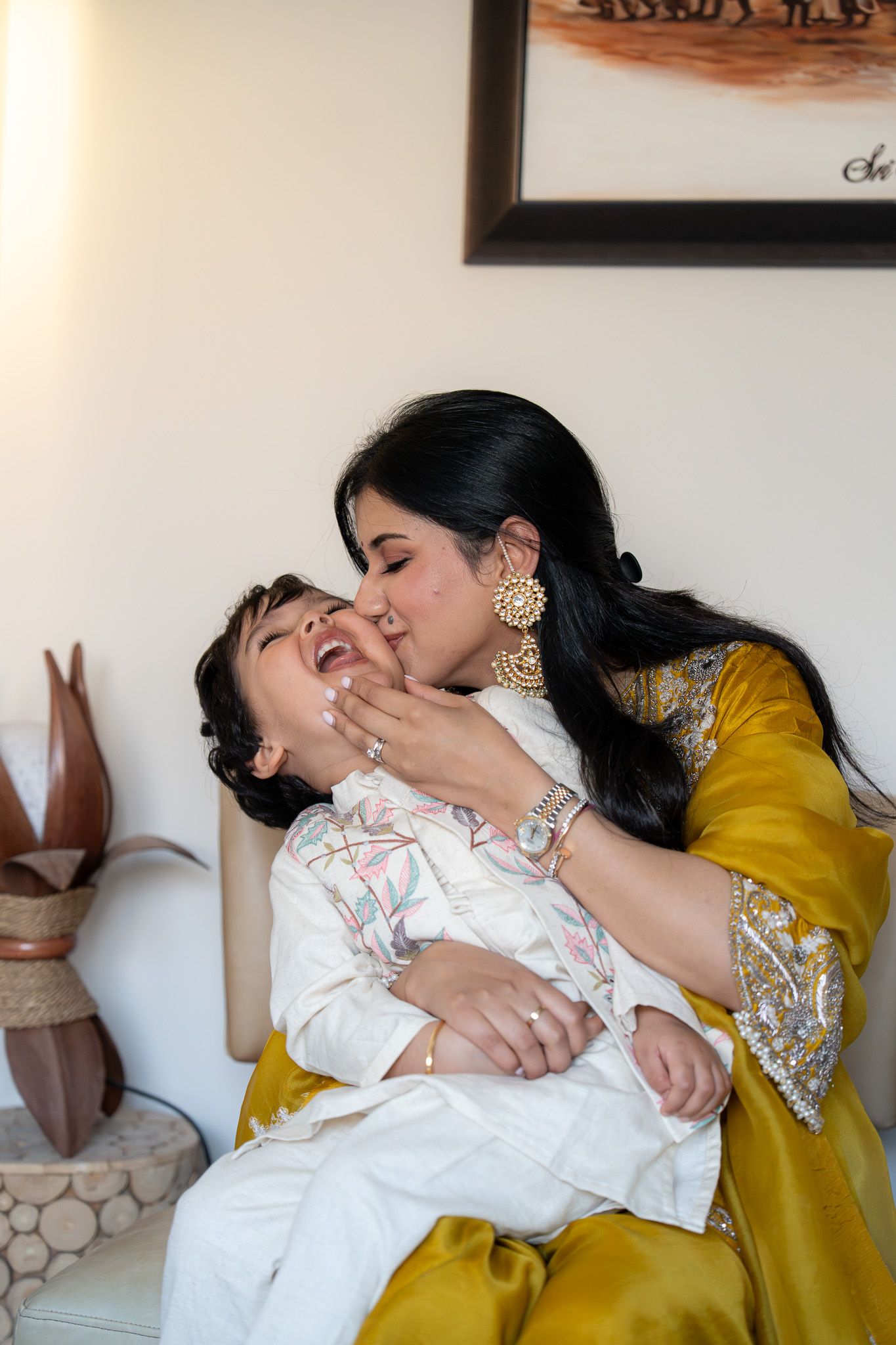 Mother kissing her laughing son Aekam while dressed in mustard yellow traditional attire during a Diwali family shoot in Auckland