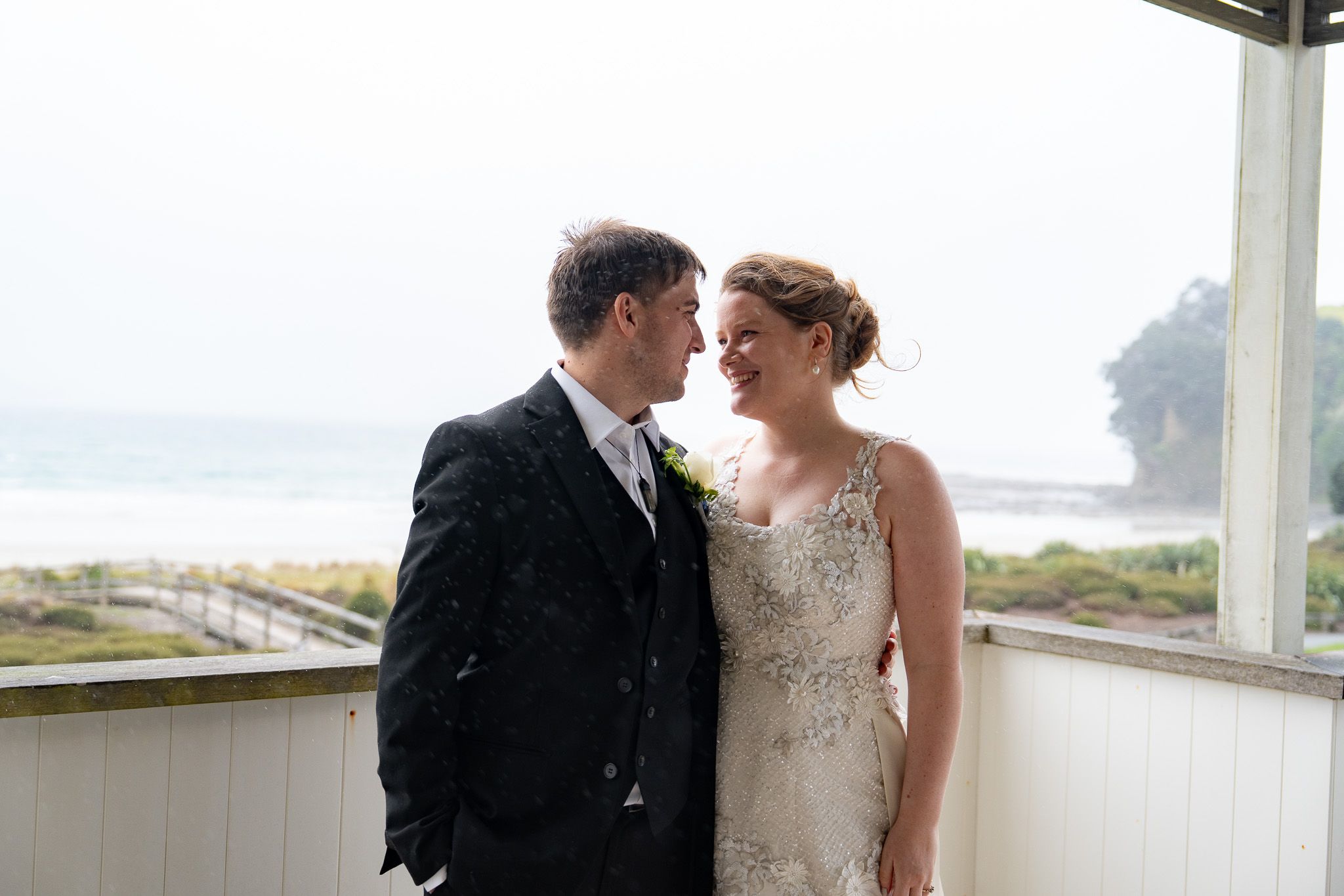 Black and white side profile of bride and groom smiling nose to nose on a covered deck by the beach