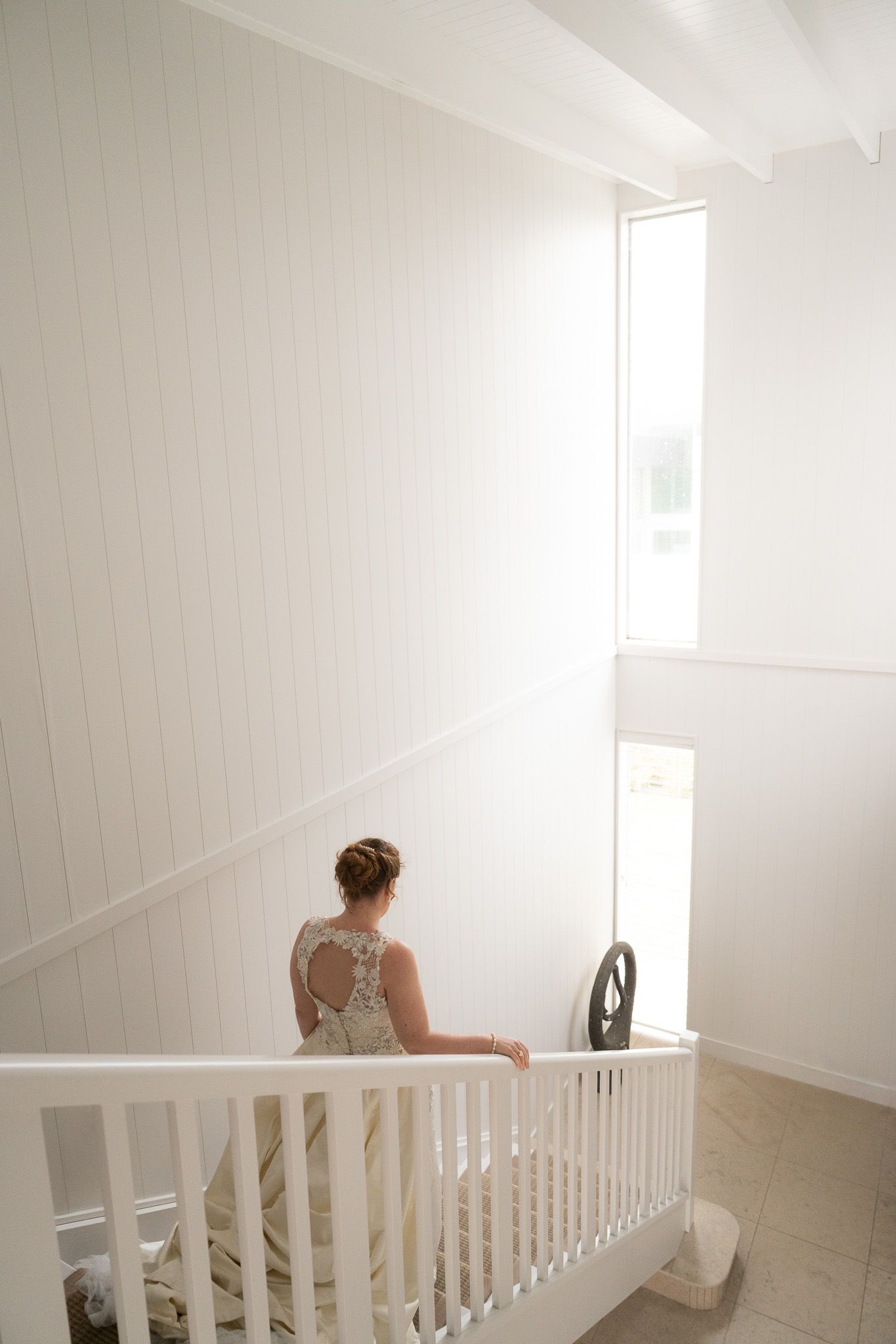Bride standing alone on a staircase landing, seen from behind near a white railing