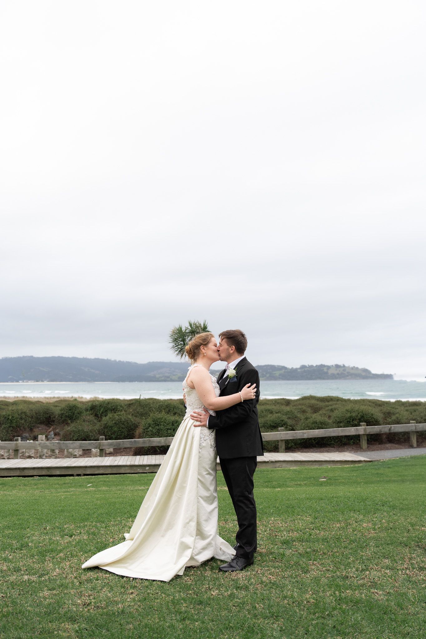 Bride and groom kissing on the lawn with the Omaha coastline and a headland in the background
