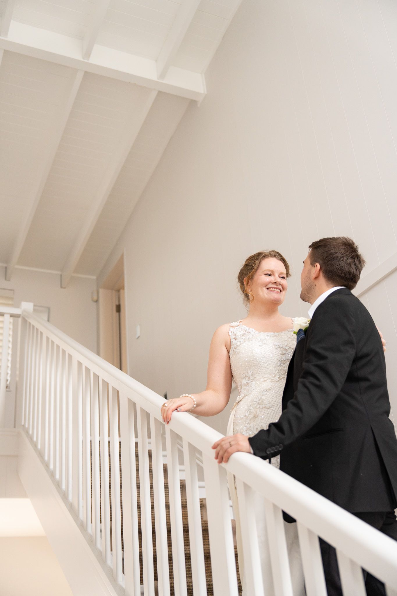 Bride and groom standing close together indoors, foreheads nearly touching, in front of a TV and fireplace
