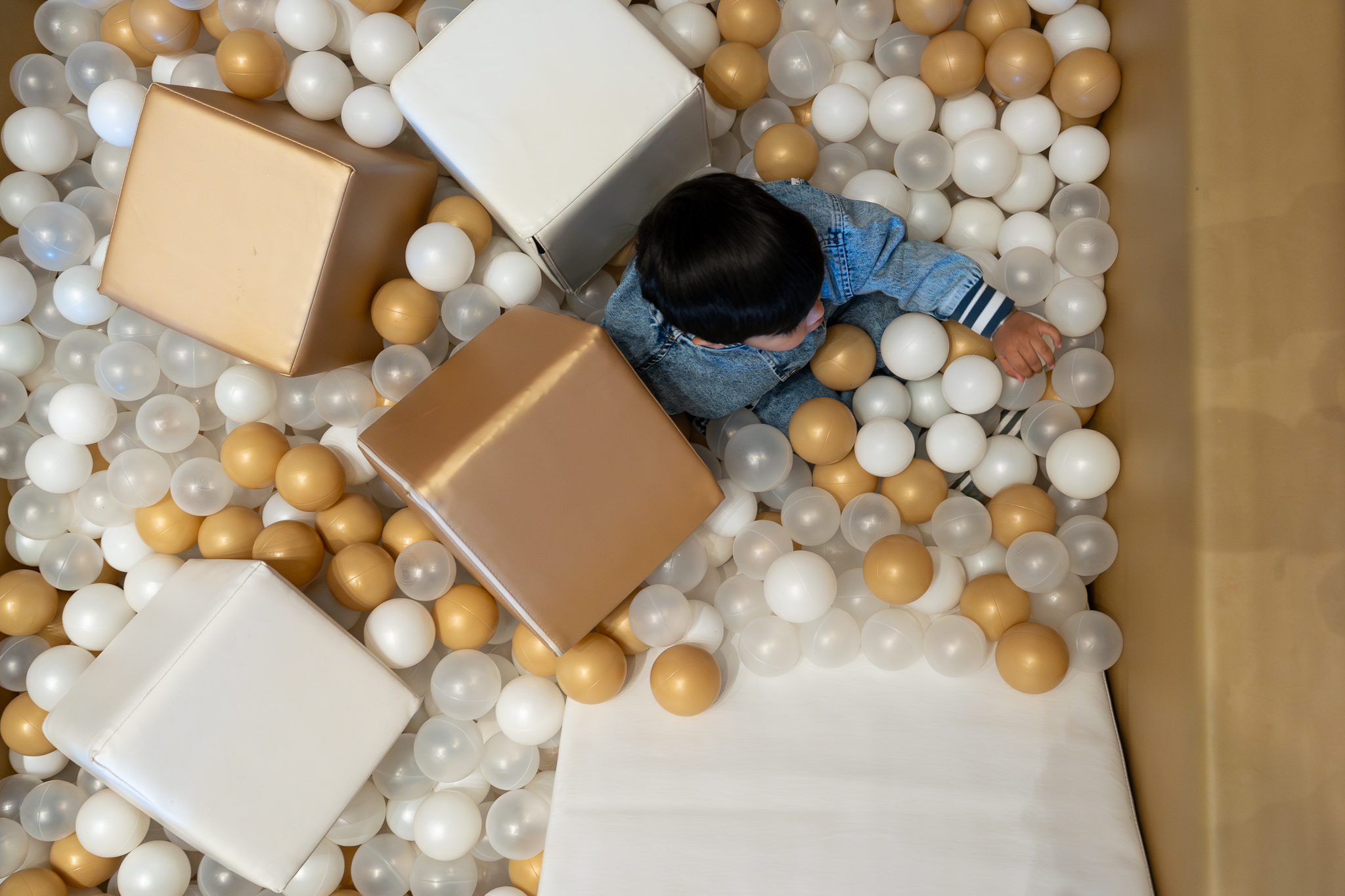 Toddler playing in a gold and white ball pit at a kids birthday party in the Razzle Dazzle Room at Naumi Auckland Airport Hotel