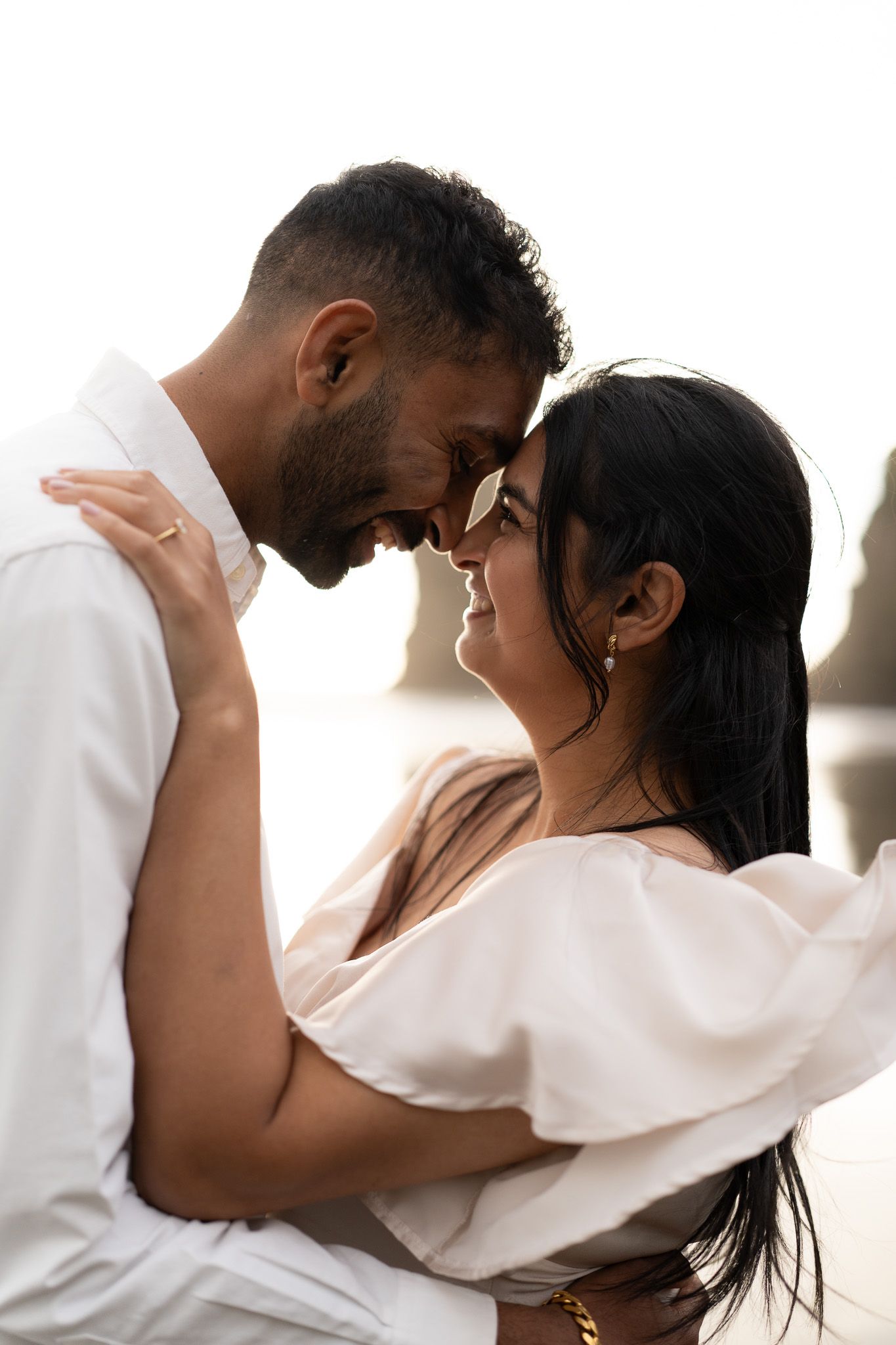Engaged couple share a forehead-to-forehead moment, smiling softly in golden light