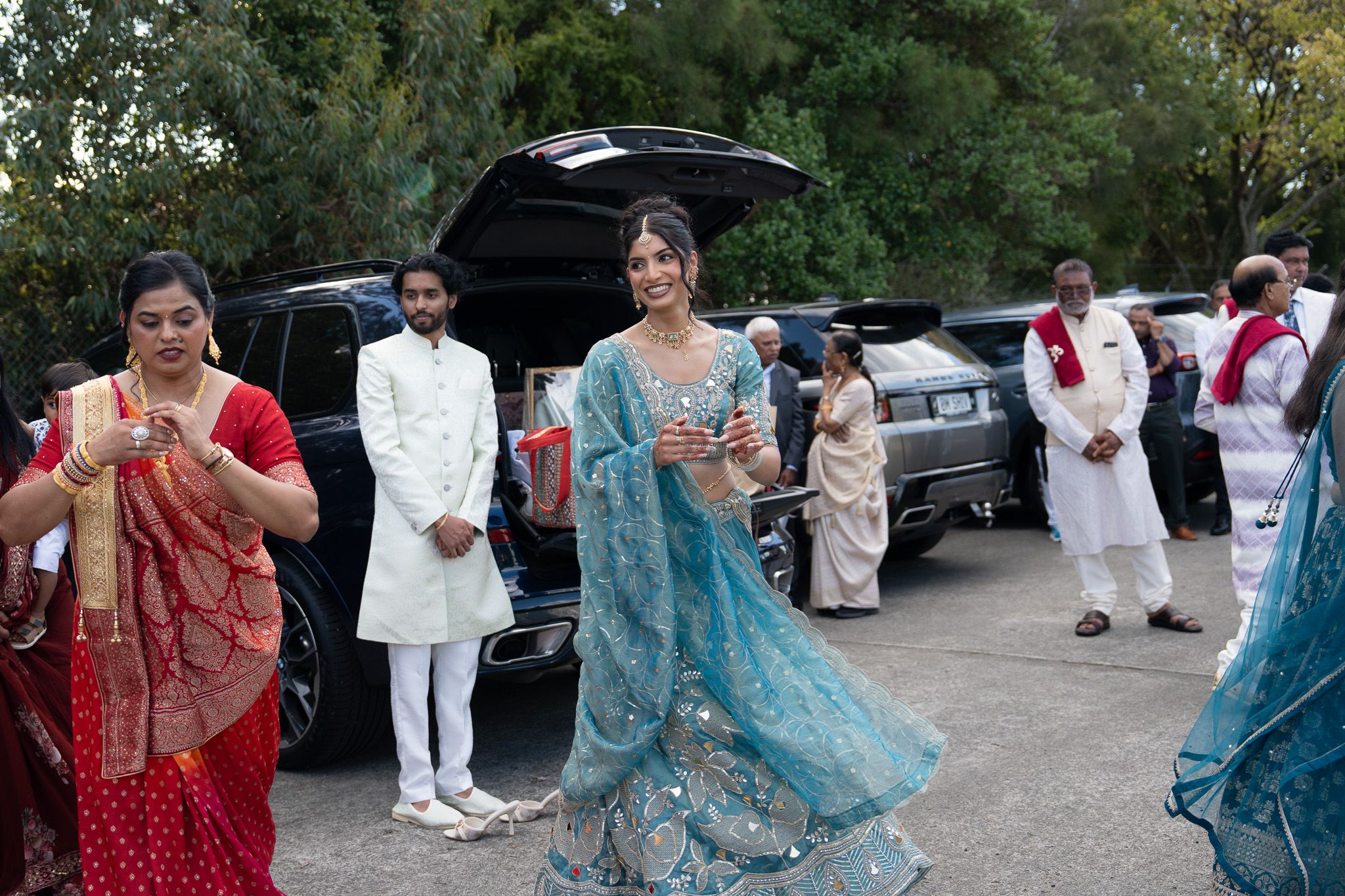 Woman performing traditional Garba dance before Mosaru ceremony in teal lehenga with family gathered outdoors during Indian wedding photography in Auckland