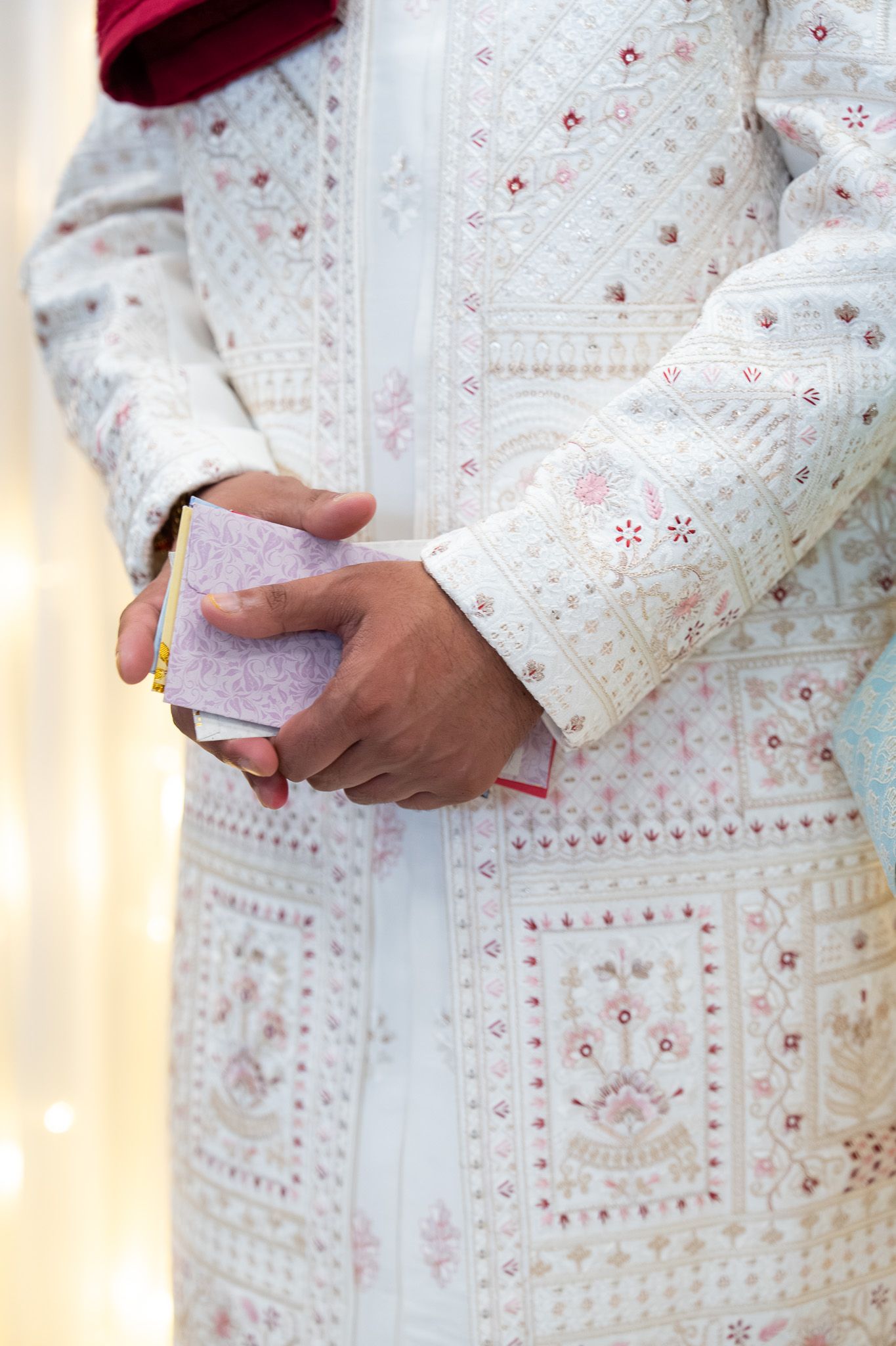 Close up of groom holding ceremonial envelopes during Indian Mosaru ritual wearing embroidered sherwani photography in Auckland