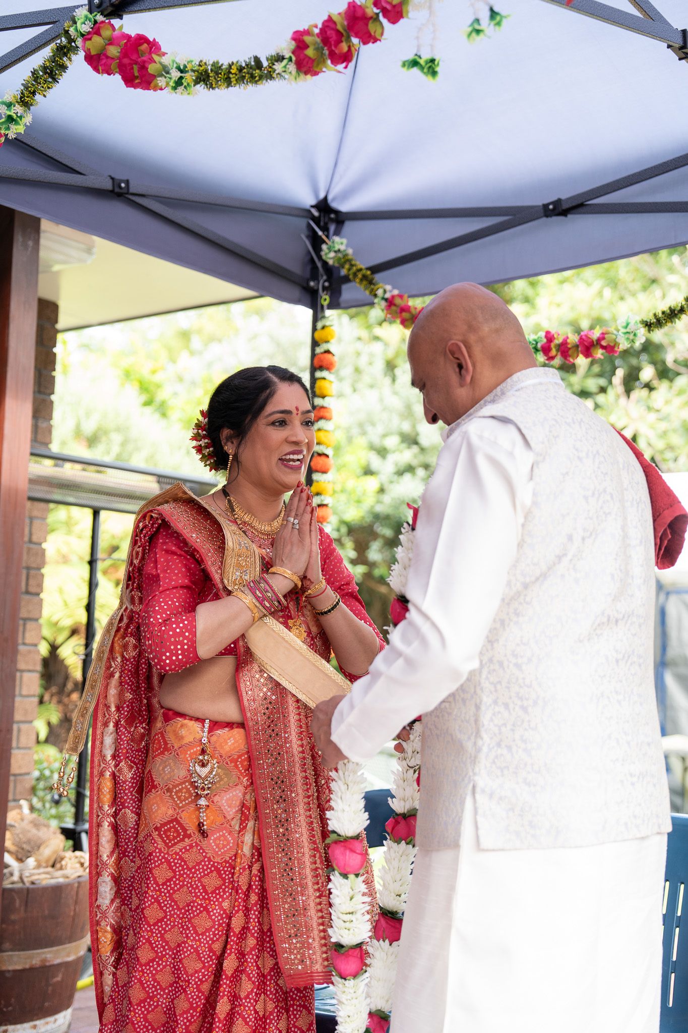 Mother greeting father during Indian pre wedding Shantak ceremony with traditional attire and garlands captured during wedding photography in Auckland