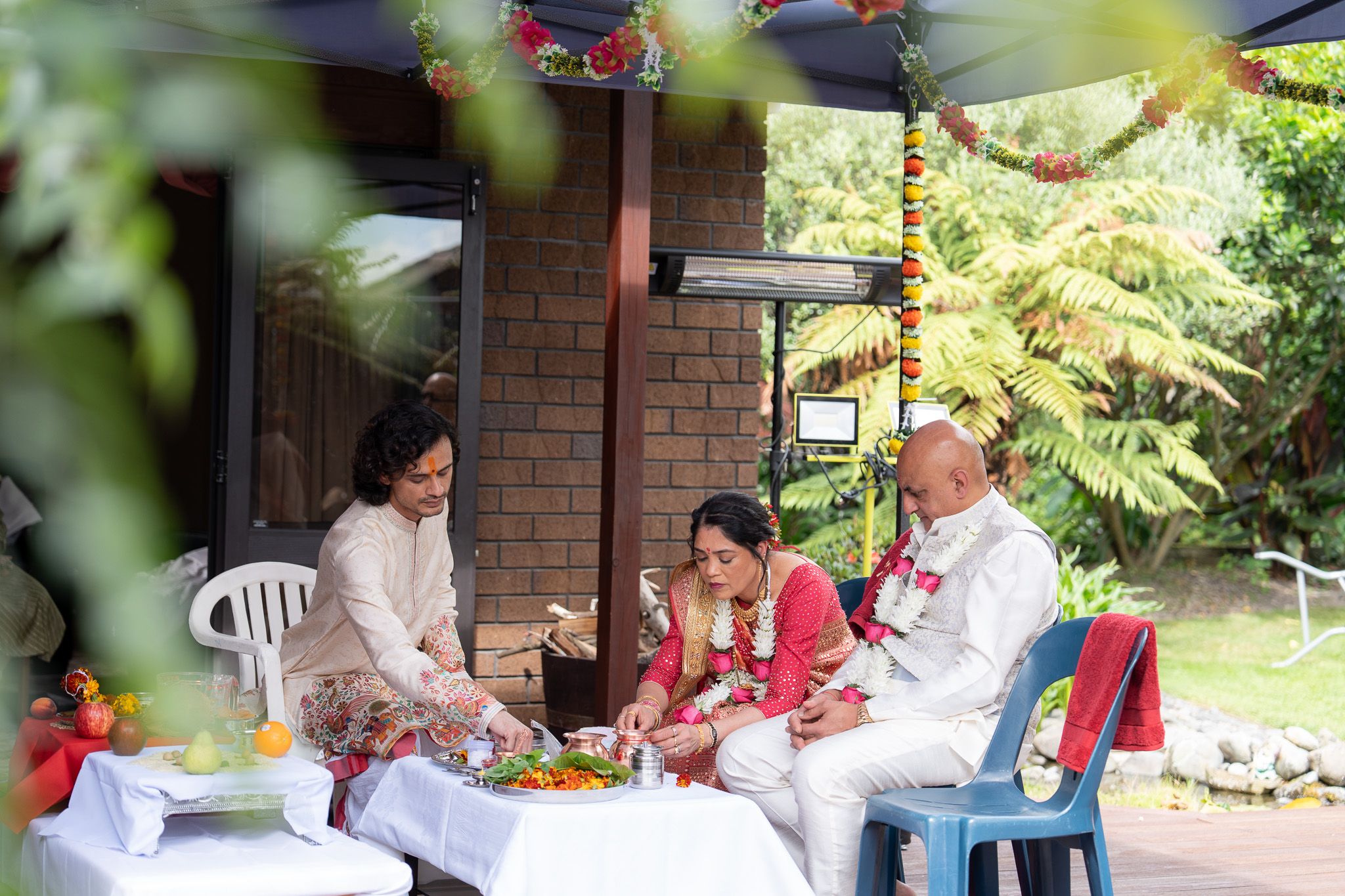 Family performing Hindu pre wedding Shantak rituals around ceremonial offerings at home during Indian wedding photography in Auckland