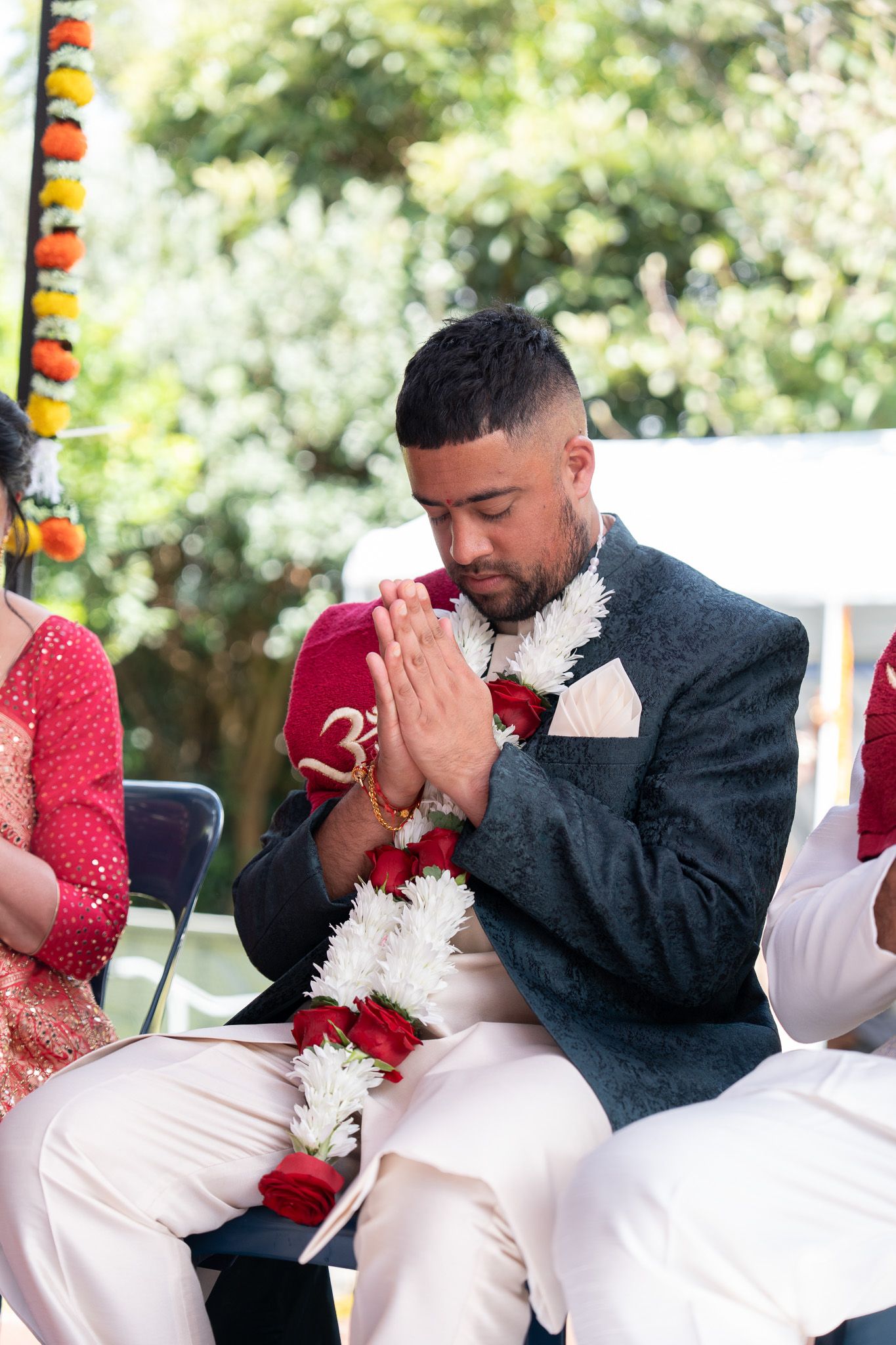 Milan seated with folded hands during his Shantak pooja ceremony with flower garlands