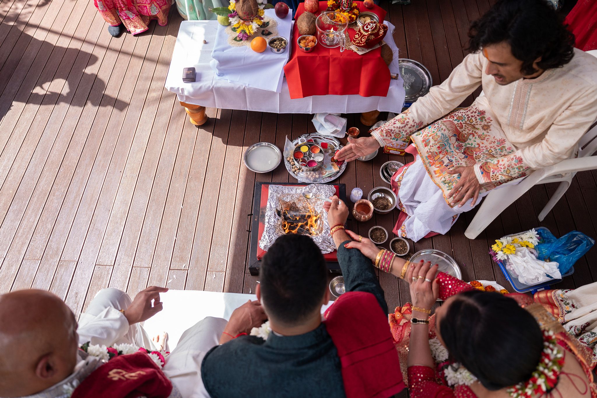 Overhead view of a Hindu fire ritual with pooja items, family and priest gathered around the havan