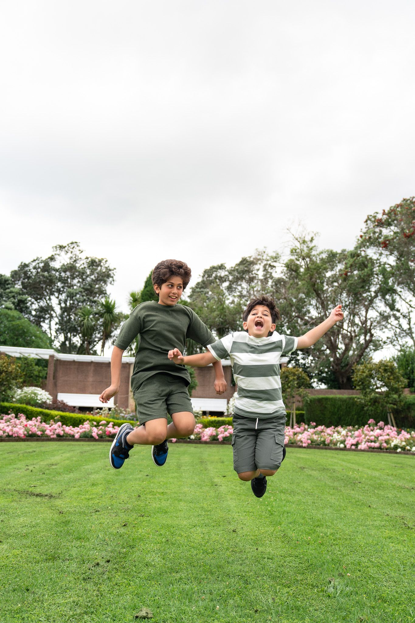 Two brothers jumping in the air on the grass during a fun family photoshoot at Michael Joseph Savage Memorial in Auckland