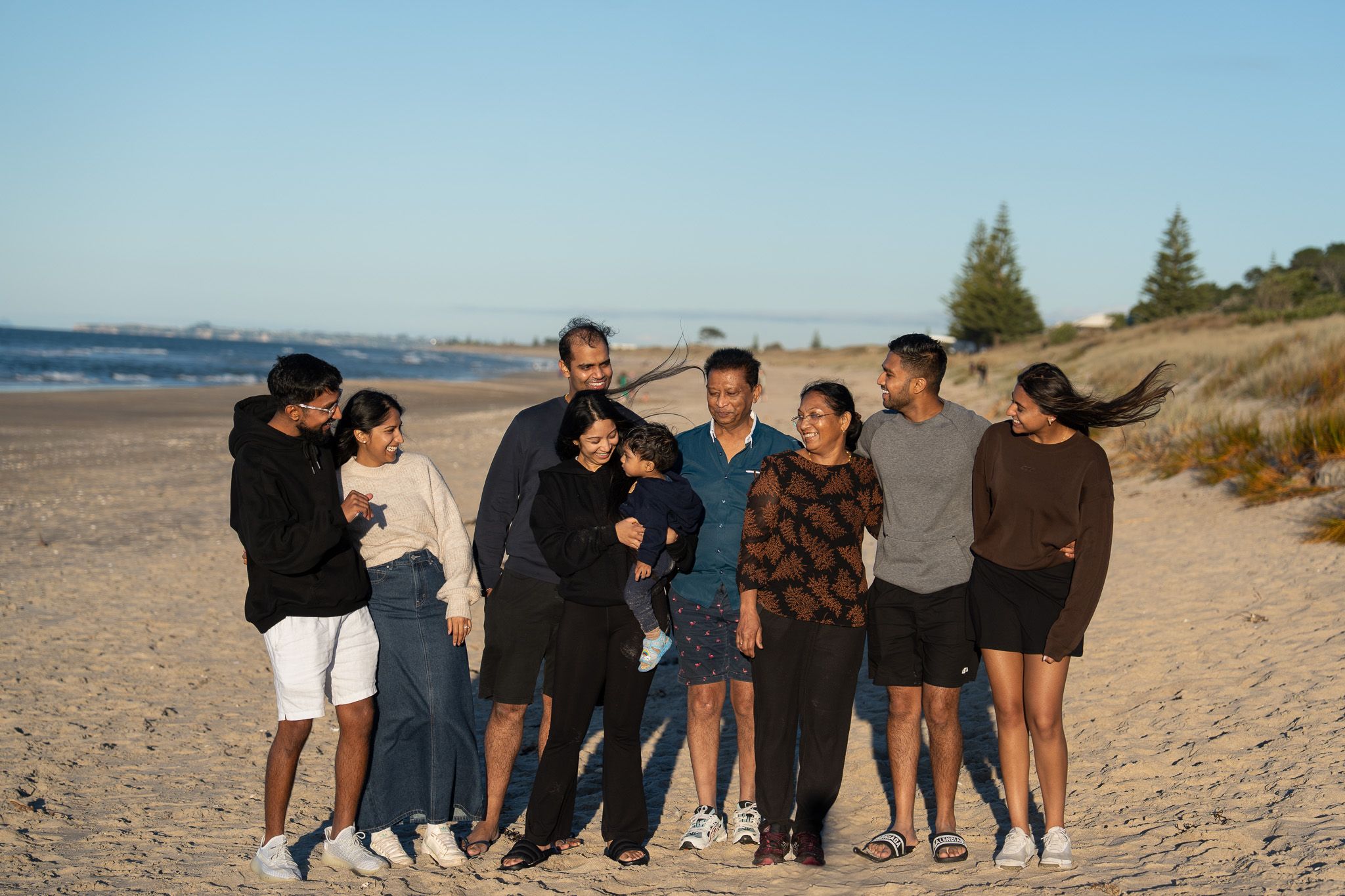 Extended family of nine walking together along a sandy beach, laughing and enjoying the moment during a golden hour family photoshoot in Auckland