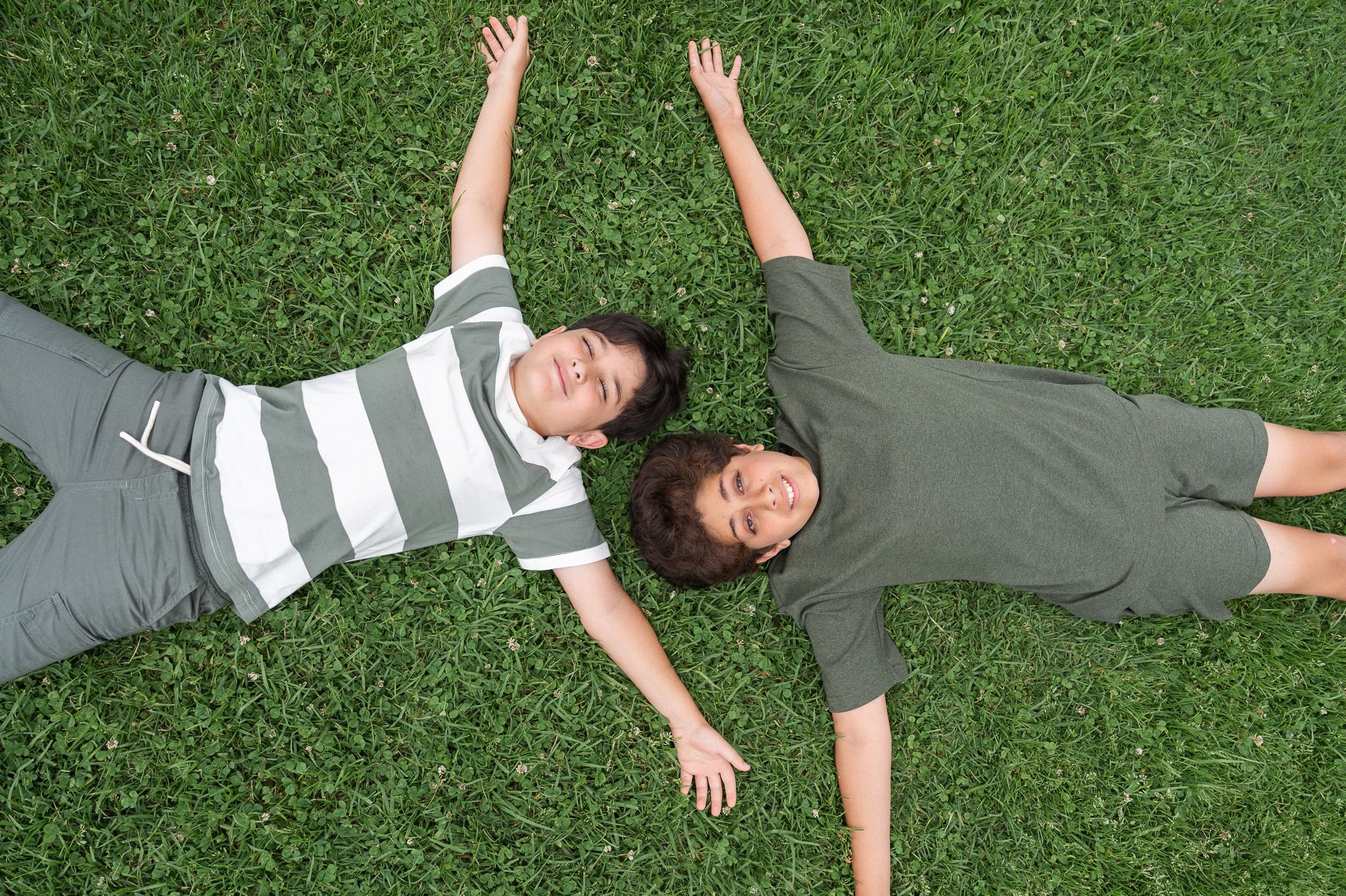 Two brothers lying on the grass with arms stretched out during a relaxed family photography session in Auckland at the Michael Joseph Savage Memorial hillside