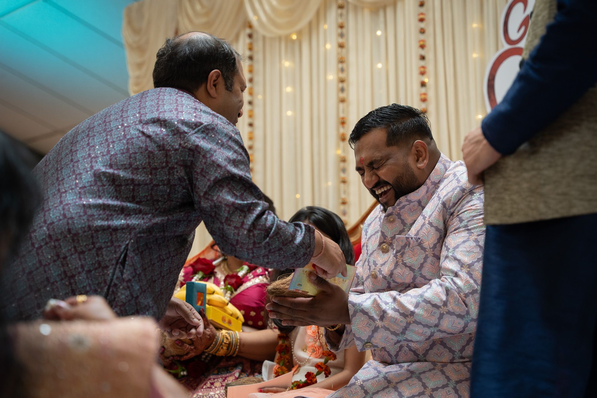 Groom laughing while receiving coconut and money as part of traditional engagement rituals during ceremony in Auckland