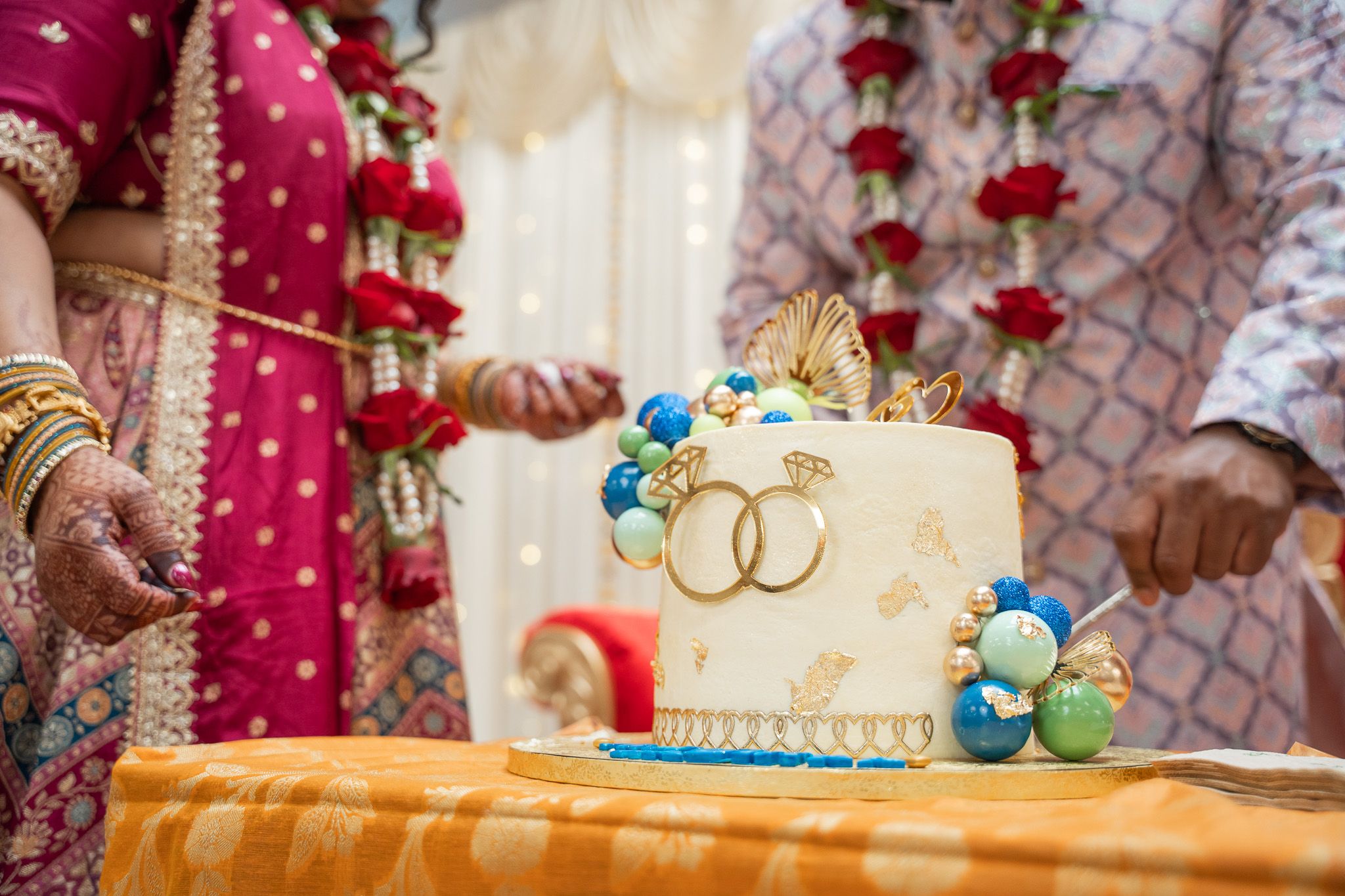 Close-up of elegant gold and blue engagement cake with ring toppers at traditional Indian engagement celebration in Auckland