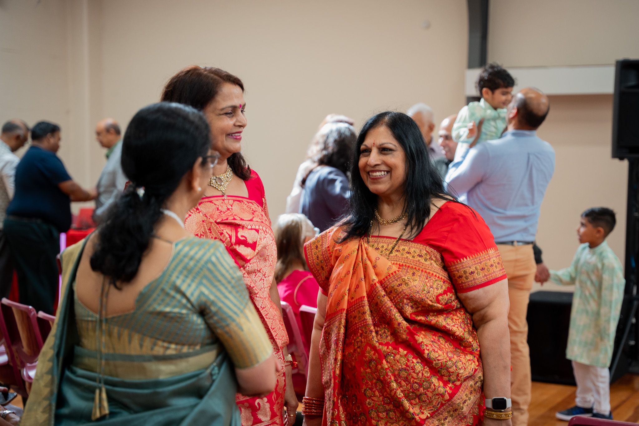 Women in vibrant saris sharing smiles and conversation during joyful Indian engagement celebration in Auckland