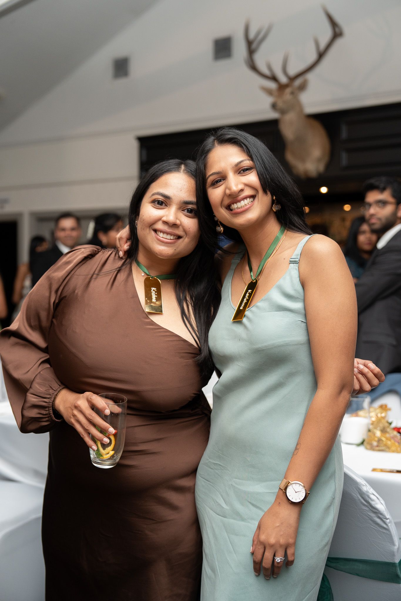Two guests smiling with drinks and name tags at Indian wedding reception Bracu Estate South Auckland candid wedding photography