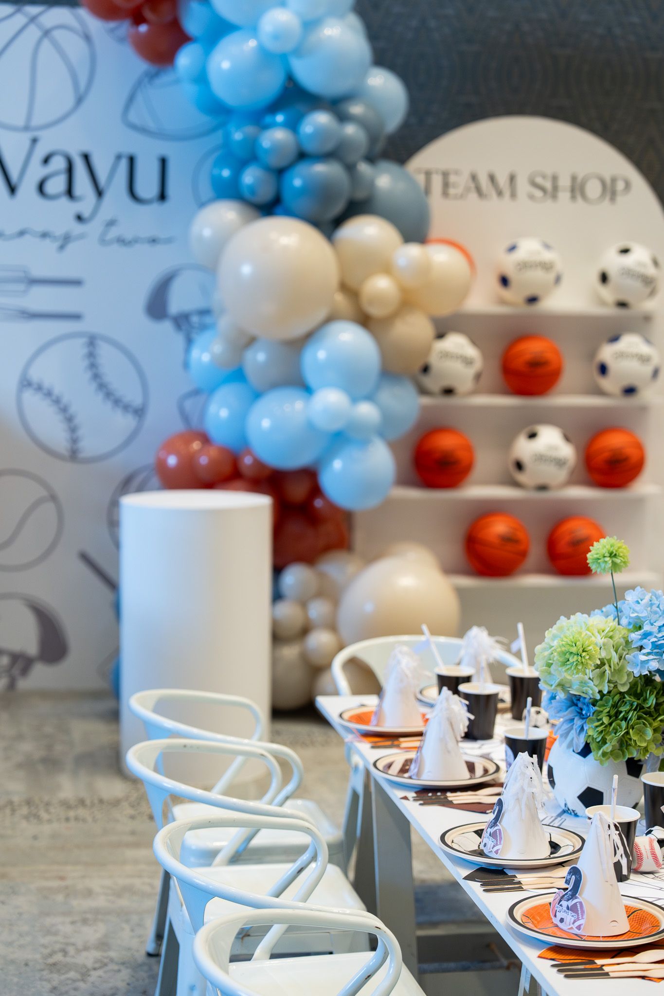 Sports themed 2nd birthday table setup with blue balloons, party hats and team shop decor at Naumi Hotel in Auckland