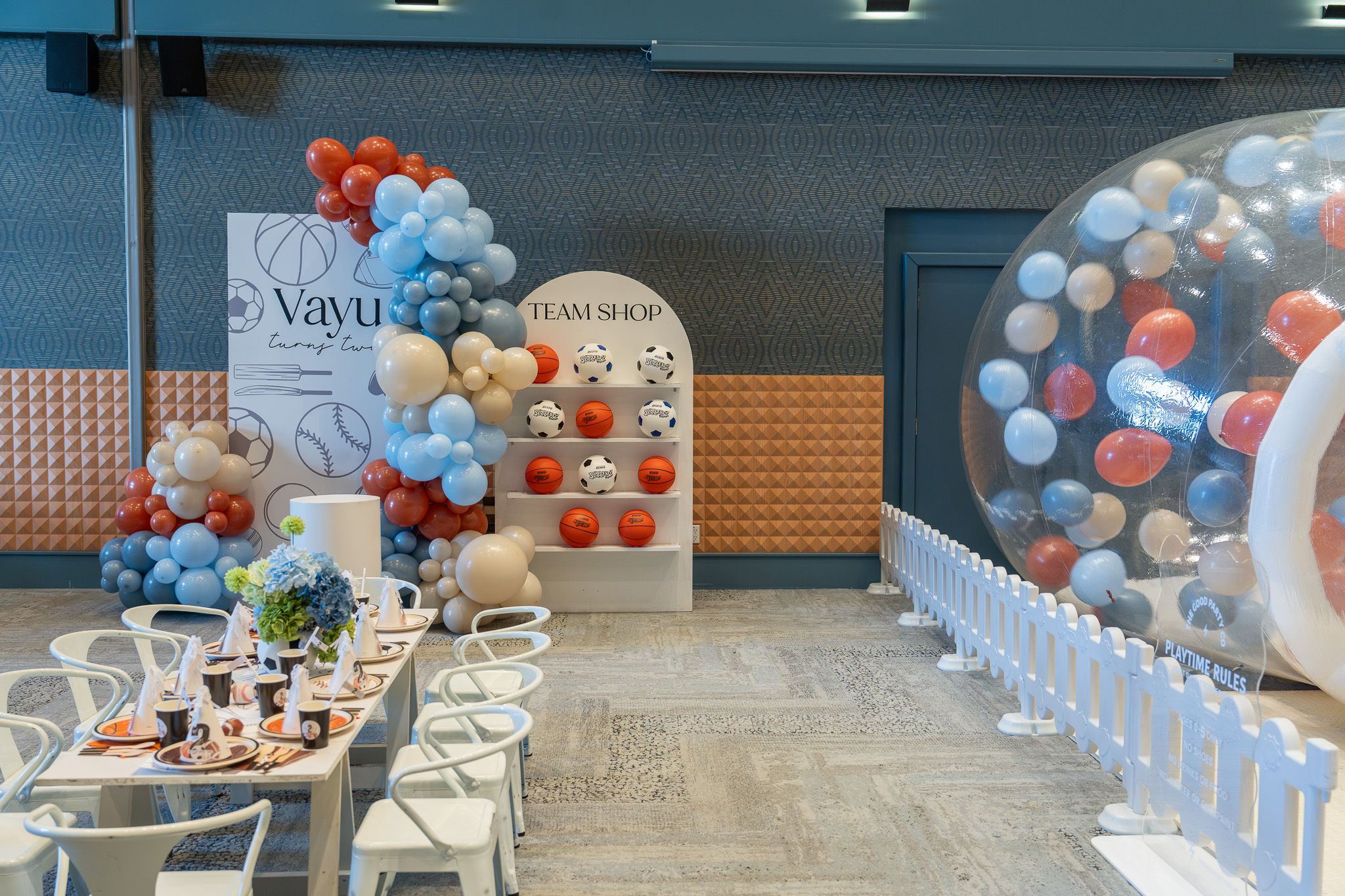 Wide view of Vayu’s sports themed 2nd birthday decorations, balloon garland, team shop display and kids’ party table