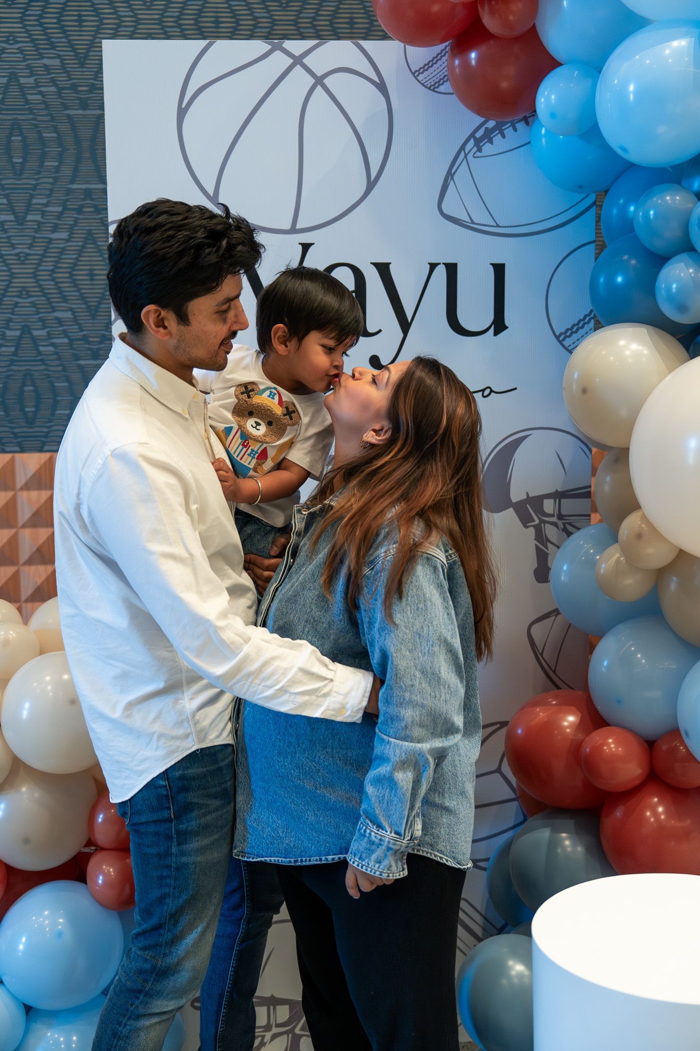 Family sharing a sweet moment under balloon decor at Vayu’s second birthday in the Razzle Dazzle Room at Naumi Auckland Airport Hotel