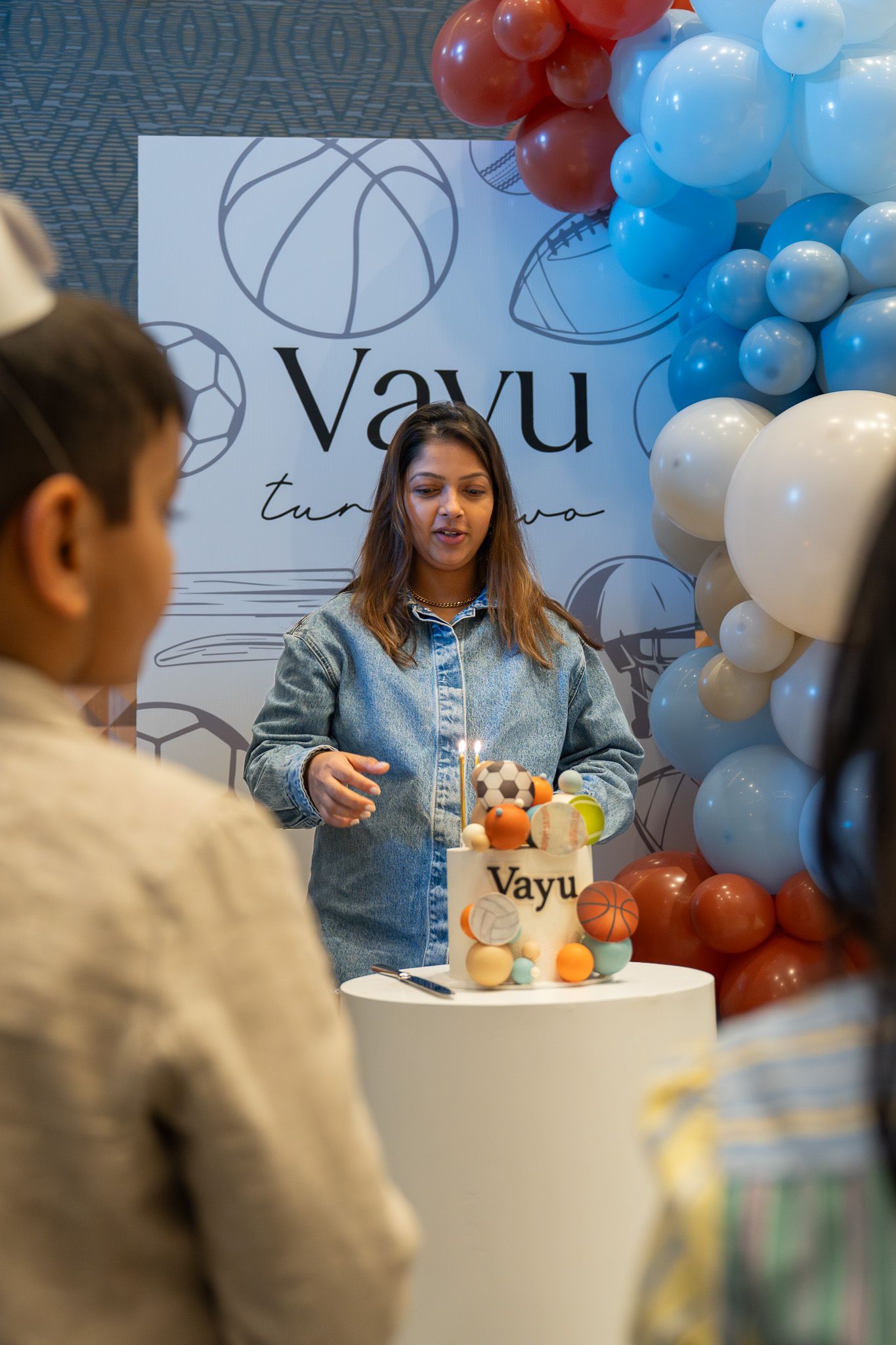 Mother preparing the cake at Vayu’s second birthday party surrounded by pastel balloons in Auckland