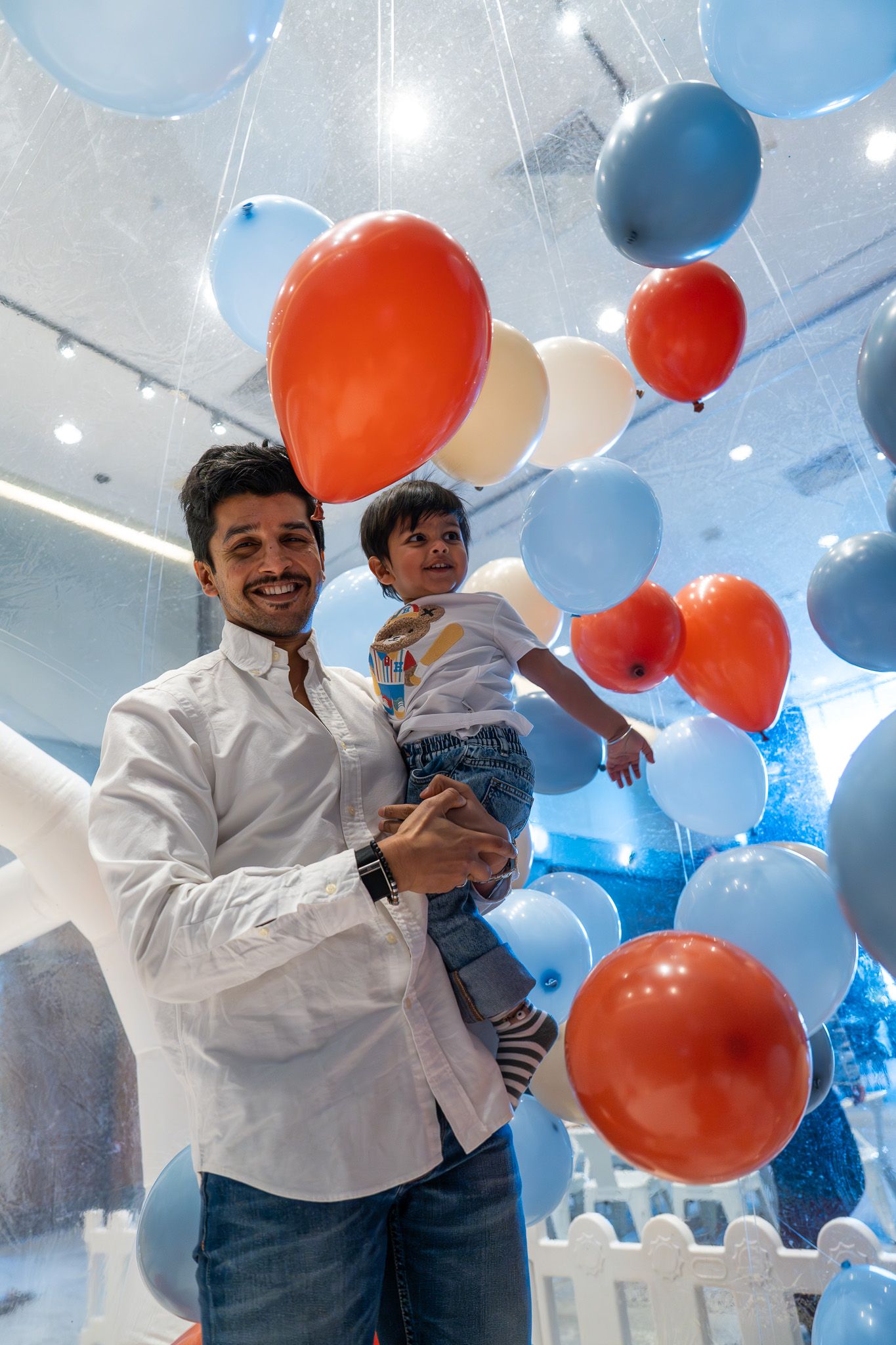 Father holding son under a ceiling of floating balloons in the Razzle Dazzle Room at Naumi Auckland Airport Hotel during a kids birthday party